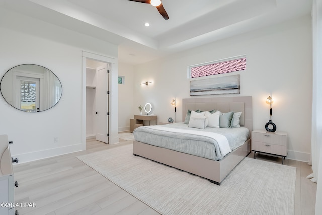 bedroom featuring light wood-type flooring, a tray ceiling, ceiling fan, and a walk in closet