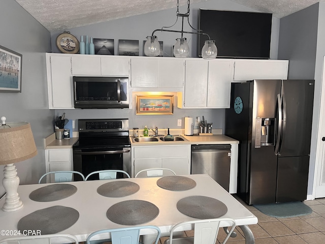 kitchen featuring sink, vaulted ceiling, decorative light fixtures, white cabinets, and appliances with stainless steel finishes