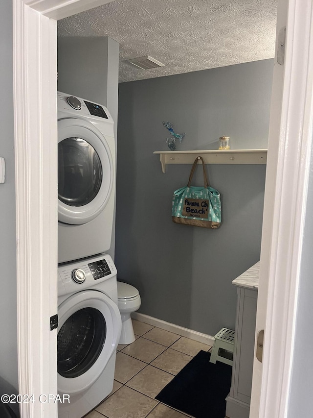 clothes washing area featuring stacked washing maching and dryer, a textured ceiling, and light tile patterned floors