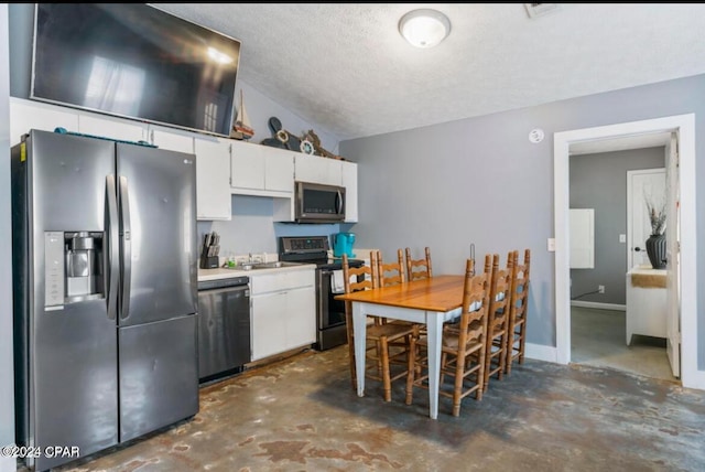 kitchen with a textured ceiling, lofted ceiling, white cabinetry, and stainless steel appliances