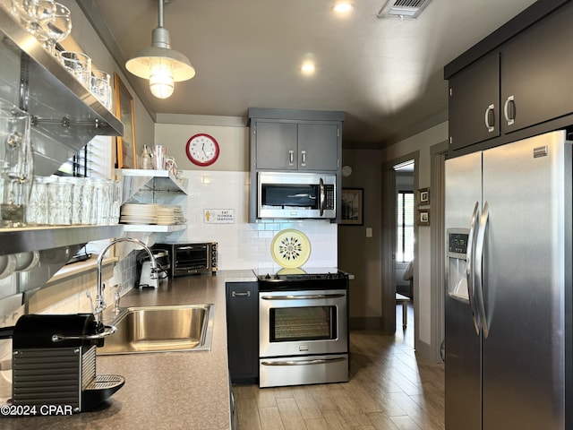 kitchen featuring sink, stainless steel appliances, tasteful backsplash, decorative light fixtures, and light wood-type flooring