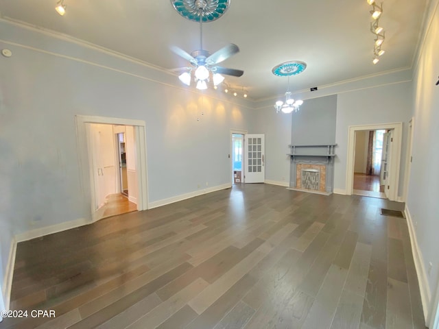 unfurnished living room featuring rail lighting, crown molding, ceiling fan with notable chandelier, and dark hardwood / wood-style flooring