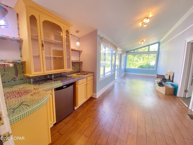 kitchen with decorative light fixtures, stainless steel dishwasher, crown molding, lofted ceiling, and light wood-type flooring