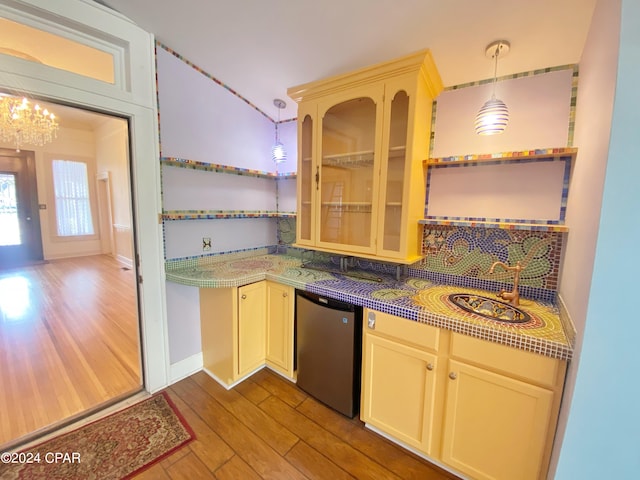 kitchen with an inviting chandelier, decorative light fixtures, dishwasher, hardwood / wood-style floors, and sink