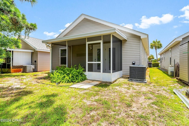 rear view of house featuring a lawn, central AC unit, and a sunroom