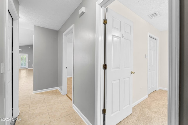 hallway featuring light tile patterned floors, visible vents, a textured ceiling, and baseboards