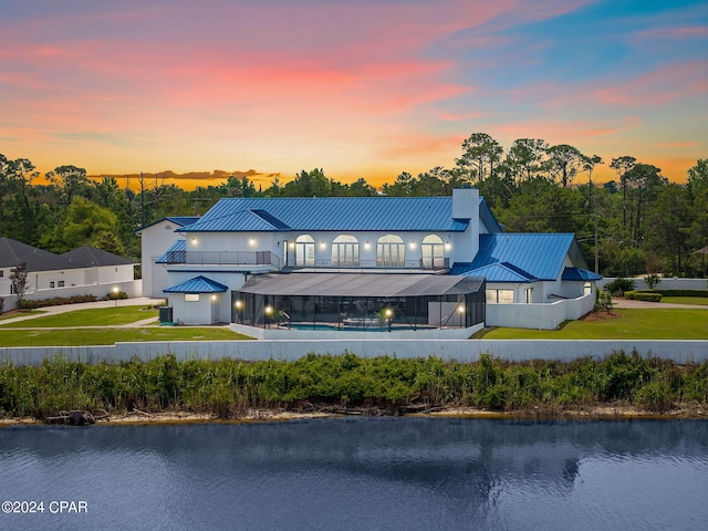 back house at dusk with a pool, a water view, and a yard