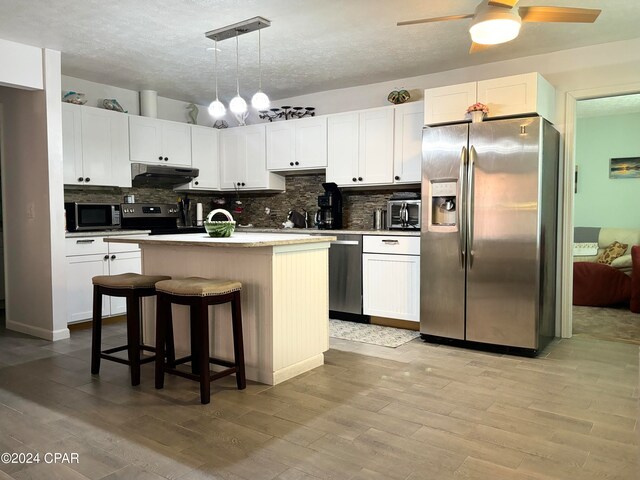 kitchen featuring stainless steel appliances, light wood-type flooring, a kitchen island with sink, white cabinets, and pendant lighting