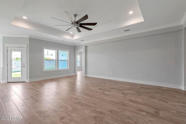 empty room featuring ceiling fan, a raised ceiling, light wood-type flooring, and crown molding