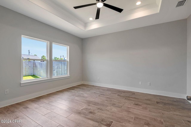 empty room with a tray ceiling, ceiling fan, light hardwood / wood-style flooring, and ornamental molding