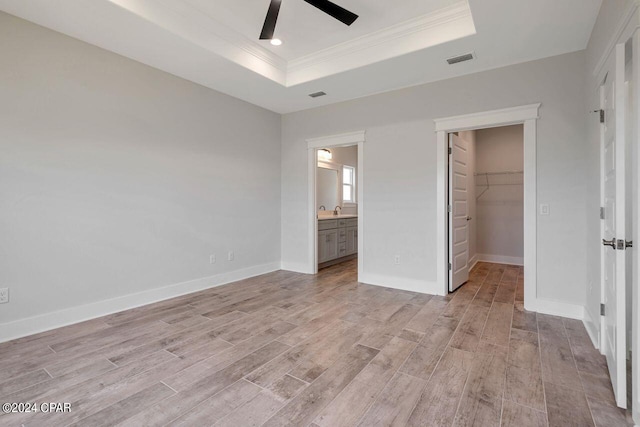 unfurnished bedroom with a walk in closet, light hardwood / wood-style flooring, ceiling fan, a tray ceiling, and a closet