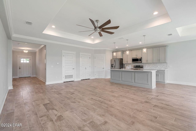 kitchen featuring a raised ceiling, light hardwood / wood-style flooring, an island with sink, gray cabinets, and appliances with stainless steel finishes