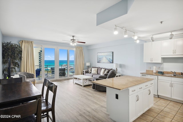 kitchen featuring a water view, white cabinetry, dishwasher, a kitchen island, and ceiling fan