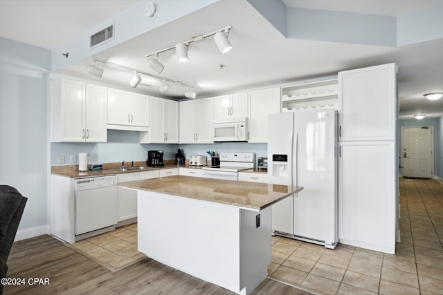 kitchen with white cabinets, light tile patterned floors, a center island, white appliances, and light stone counters