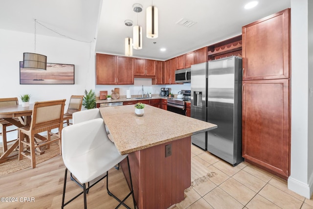 kitchen featuring sink, a center island, pendant lighting, stainless steel appliances, and light stone countertops