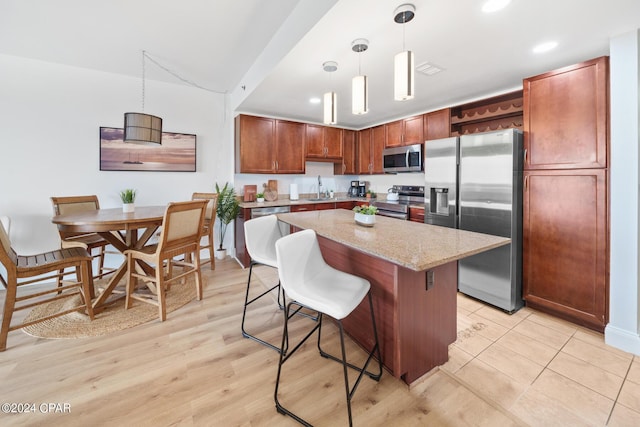 kitchen featuring decorative light fixtures, a kitchen island, a breakfast bar area, and appliances with stainless steel finishes