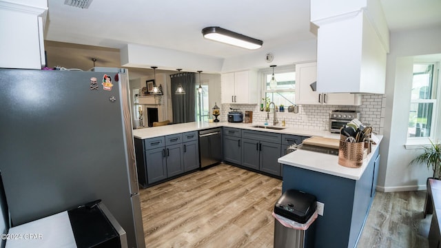 kitchen featuring sink, stainless steel appliances, kitchen peninsula, pendant lighting, and white cabinets