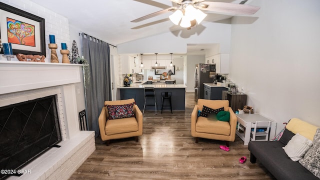 living room with a brick fireplace, vaulted ceiling, ceiling fan, and dark wood-type flooring