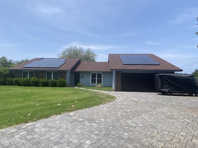 ranch-style home with solar panels, a garage, and a front lawn