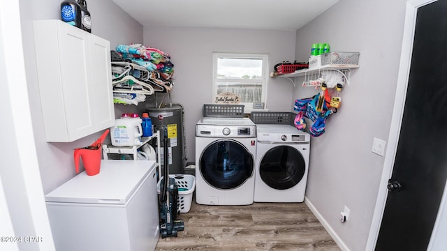 clothes washing area featuring cabinets, light hardwood / wood-style floors, washer and clothes dryer, and water heater