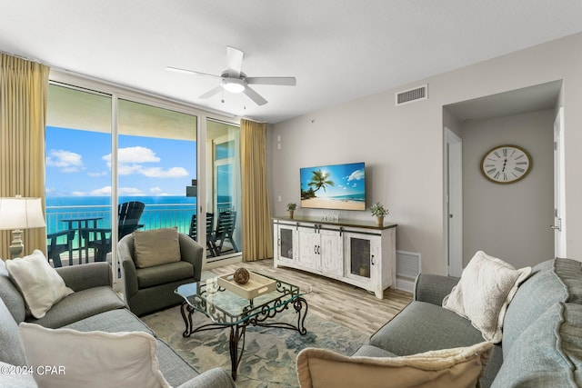 living room with floor to ceiling windows, wood-type flooring, ceiling fan, and a water view