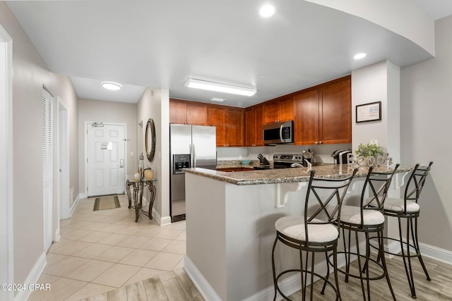 kitchen featuring stainless steel appliances, kitchen peninsula, stone counters, a kitchen bar, and light tile floors