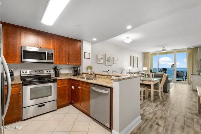 kitchen featuring light stone countertops, light wood-type flooring, stainless steel appliances, kitchen peninsula, and sink