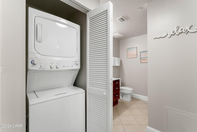 clothes washing area featuring stacked washer and clothes dryer and light tile floors