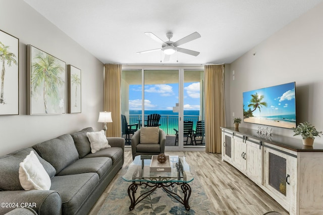 living room featuring light hardwood / wood-style floors, floor to ceiling windows, ceiling fan, and a water view