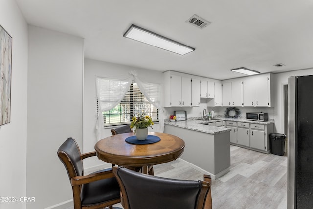 kitchen featuring white cabinetry, sink, light stone countertops, appliances with stainless steel finishes, and light hardwood / wood-style flooring