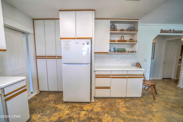 kitchen featuring tasteful backsplash, a textured ceiling, white cabinets, dark tile patterned flooring, and white refrigerator