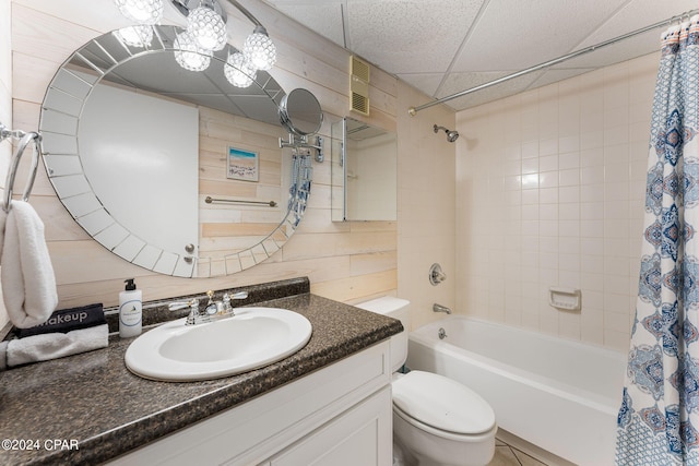 full bathroom with toilet, wood walls, a paneled ceiling, shower / bath combination with curtain, and vanity