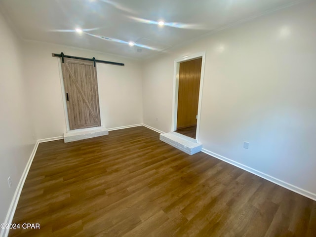 unfurnished room featuring a barn door, dark hardwood / wood-style flooring, and ornamental molding