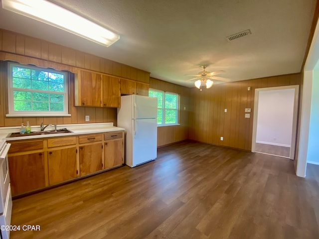 kitchen with ceiling fan, sink, white refrigerator, light hardwood / wood-style flooring, and wood walls