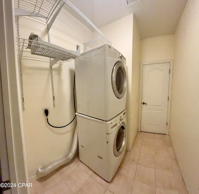 laundry area with light tile patterned floors and stacked washing maching and dryer