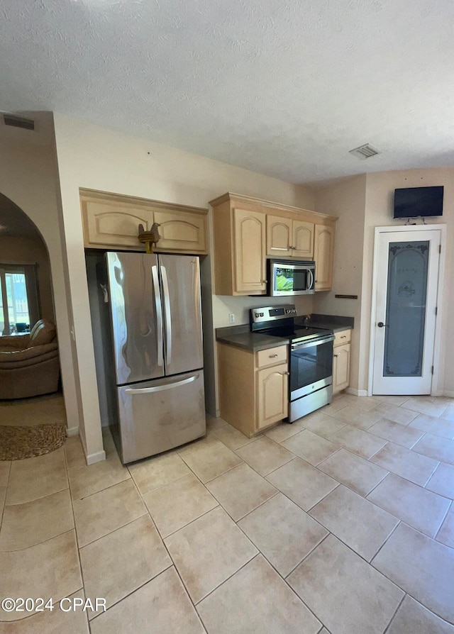 kitchen featuring light brown cabinets, light tile patterned floors, stainless steel appliances, and a textured ceiling