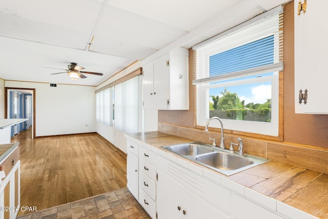 kitchen with a sink, a ceiling fan, white cabinetry, baseboards, and tile counters