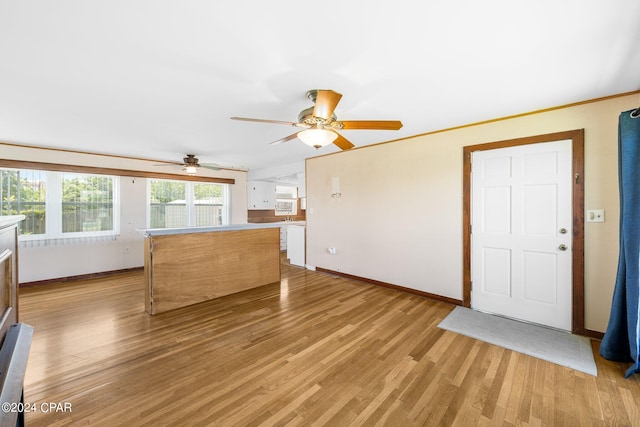 unfurnished living room with a ceiling fan, light wood-type flooring, ornamental molding, and baseboards