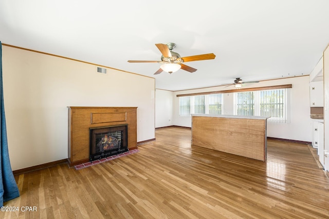 unfurnished living room with ornamental molding, light wood-type flooring, a warm lit fireplace, and visible vents