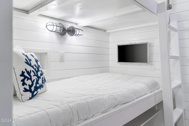 bedroom featuring beam ceiling and wood walls