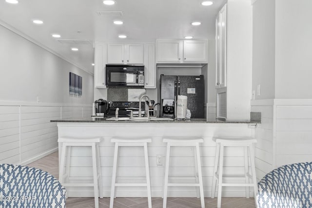 kitchen featuring kitchen peninsula, light hardwood / wood-style flooring, white cabinetry, black appliances, and dark stone counters