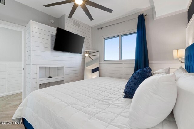 bedroom featuring light parquet flooring, wooden walls, and ceiling fan