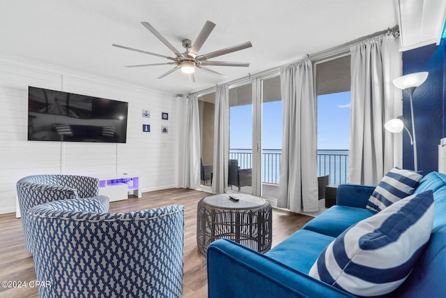 living room featuring wooden walls, a water view, ceiling fan, and hardwood / wood-style flooring