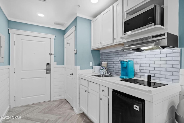 kitchen with sink, white cabinets, wall chimney exhaust hood, black appliances, and light parquet flooring