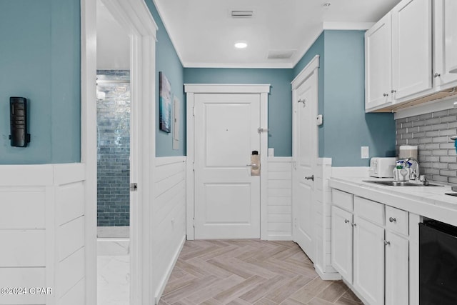 kitchen with dishwasher, sink, light parquet flooring, and white cabinetry