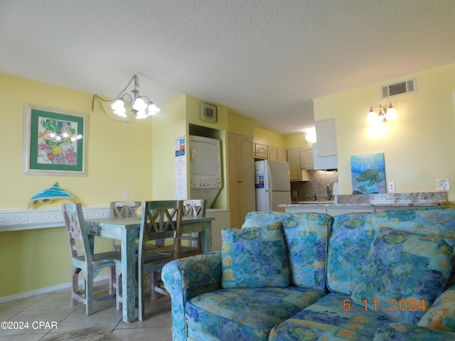 tiled living room with stacked washer / dryer, a textured ceiling, and an inviting chandelier