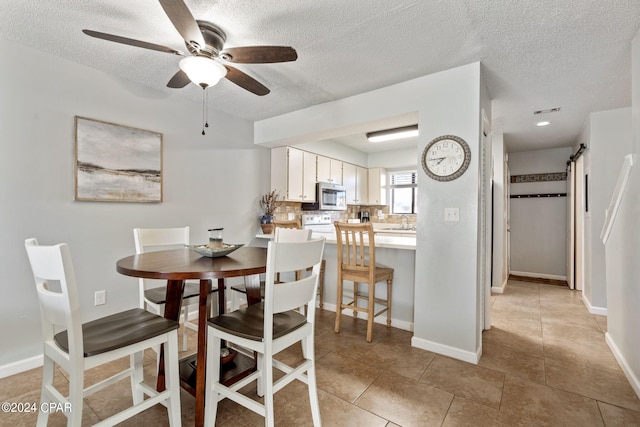 dining room featuring ceiling fan, a barn door, sink, a textured ceiling, and light tile patterned floors