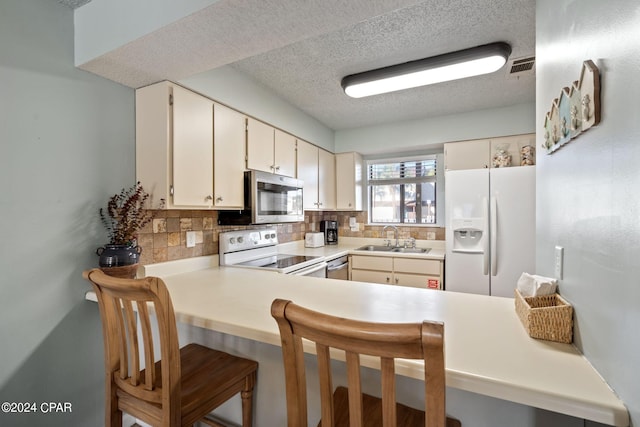 kitchen with kitchen peninsula, stainless steel appliances, tasteful backsplash, a textured ceiling, and sink