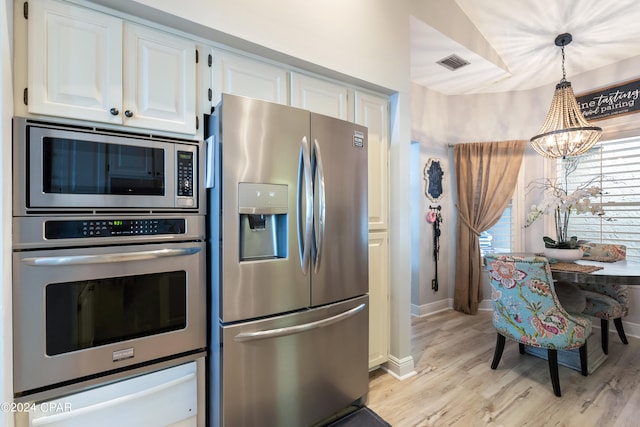 kitchen featuring appliances with stainless steel finishes, pendant lighting, an inviting chandelier, light hardwood / wood-style flooring, and white cabinetry