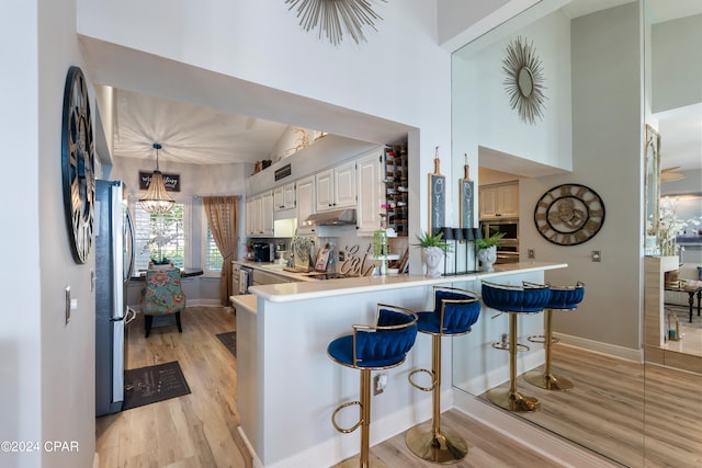 kitchen with kitchen peninsula, a breakfast bar, a notable chandelier, light hardwood / wood-style floors, and white cabinetry